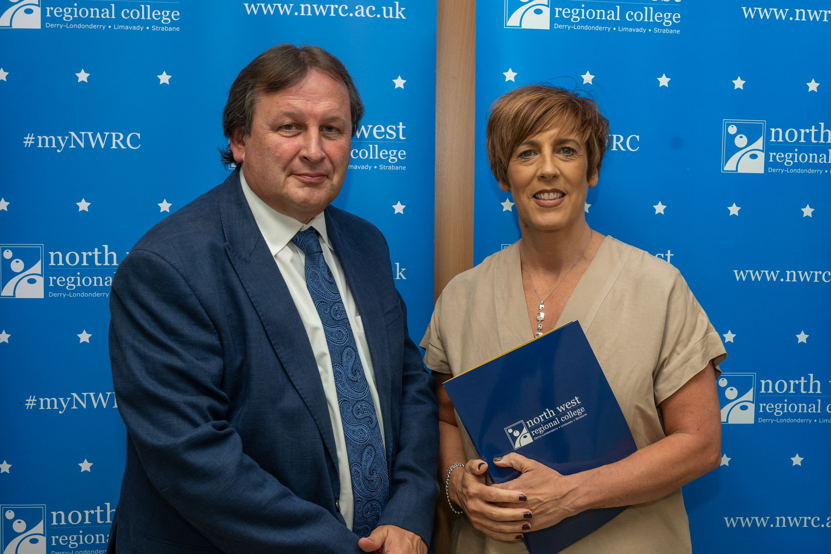 Man and woman in front of a NWRC blue screen holding a presentation holder.