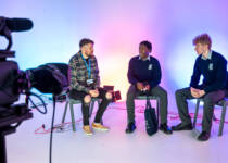 two schoolboys sitting in a film production studio chatting with a lecturer