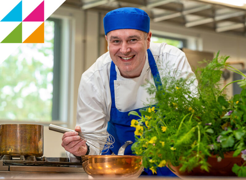 Male chef smiling while whisking liquid in a bowl in a catering kitchen