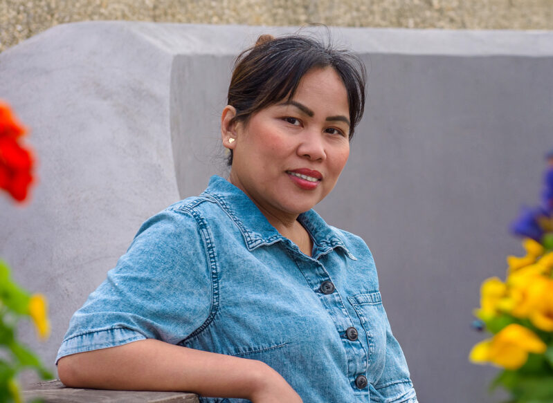 Filipino woman leans against a bench with flowers in foreground