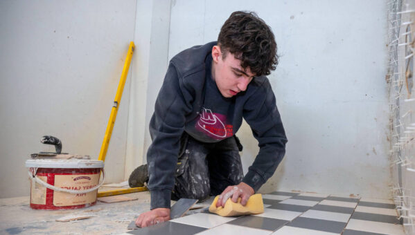 young male tiler kneeing while placing black and white tiles on the floor