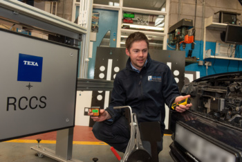 Male in mechanic overalls beside a car engine