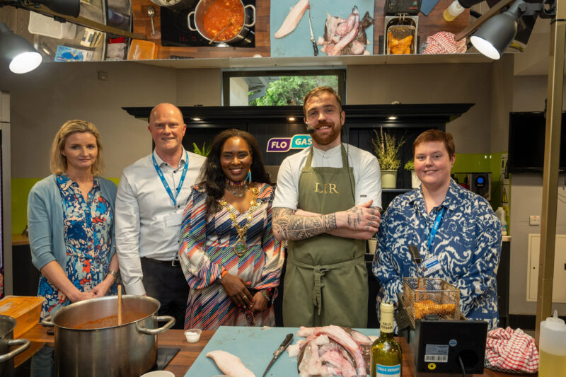 group of five stand in a demo kitchen with raw fish on the boards in front of them.