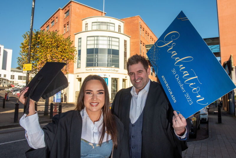 A man and woman wearing graduation gowns and mortar boards outside NWRC's Strand Road campus.