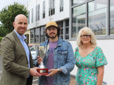 Student is presented with award outside the college building. Also pictured are two other people