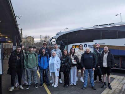 12 students and two lecturers holding luggage beside a coach