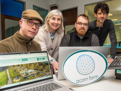 Four people in front of laptops and a sign with Acorn farm written on it