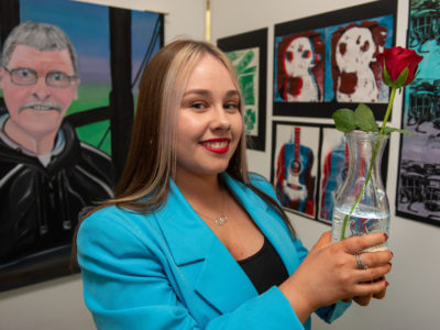 Female student in blue jacket in front of Art holding a vase with a flower