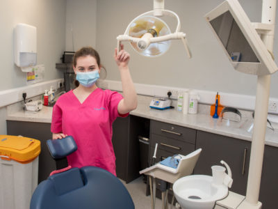 Dental nurse pictured in dental surgery wearing a mask and holding on to the dental chair