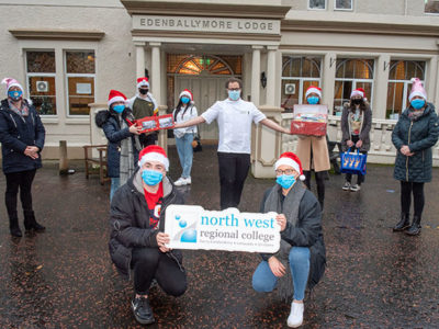 Group of students standing outside care home wearing Santa hats and face coverings