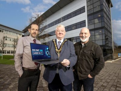 Three men pictured outside a college building holding a laptop