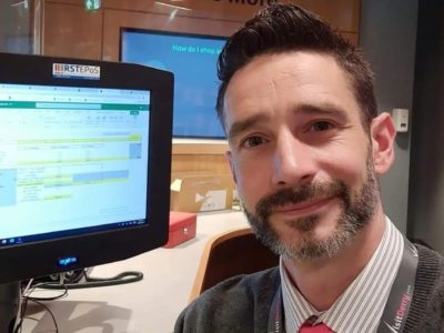 Man with a beard smiling. He is sitting in an office in front of a computer