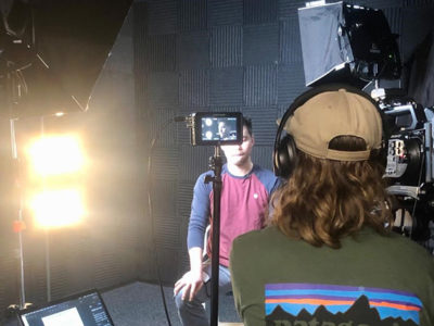 Two male students in film studio with camera and lighting equipment