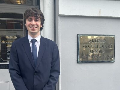 man in a suit standing outside an office with a gold plate that states McDaid, McCullough and Moore.