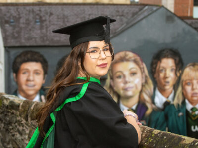 NWRC student in graduation gown and hat picture at the iconic Derry girls mural