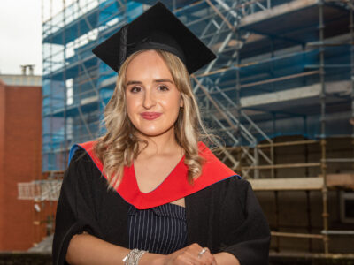 woman pictured in graduation gowns outside a building site