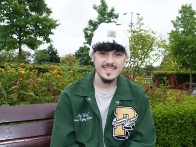 A young man in a white hat sits in a garden. He is wearing a white hat