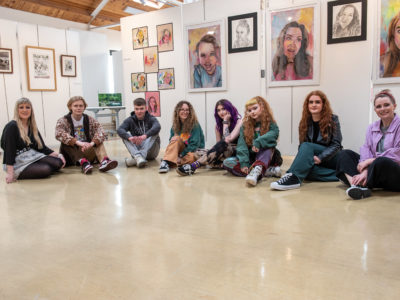 group of Art & Design students sitting on the floor with their artwork displayed on the walls