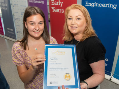 A female lecturer with a female student at an awards ceremony. The two of them are holding a certificate.