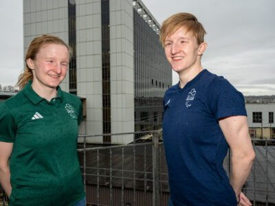 Two Athletes in a green and navy t-short outside the college buildings