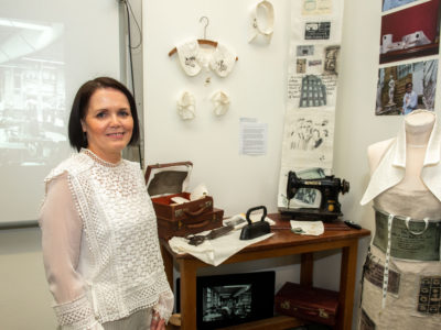 Student in front of her art work which includes a mannequin, sewing machine and prints on the wall.