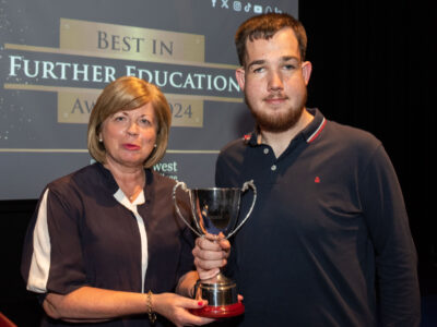 Woman and man on a stage holding a trophy. The screen behind says Best in Further Education awards 2024