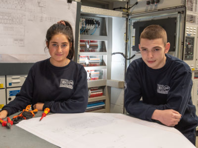 Young male and female electricians in the warehouse with plans in front of them and tools to the side