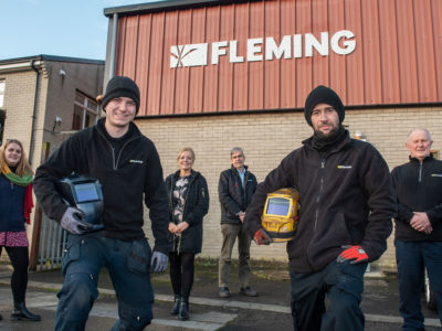 group of people outside a building, with the word Fleming - the two men at the front are holding welding hoods