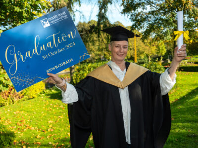 Woman in a graduation gown and hat holding a graduation sign