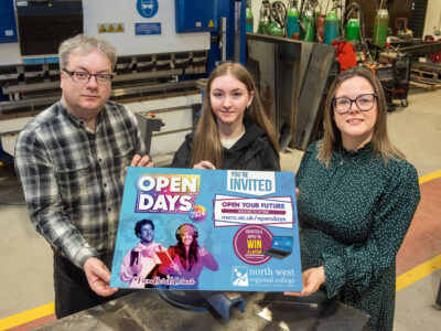 Three people in a welding workshop holding a sign for Open day