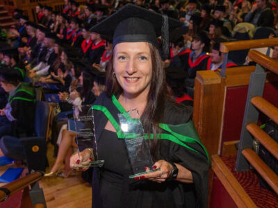women in graduation gown holding a trophy