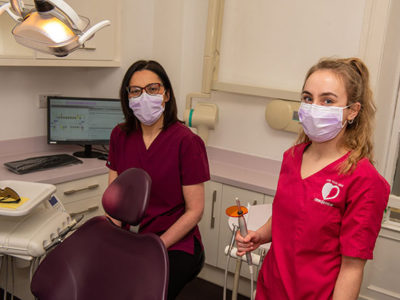 Dentist and dental nurse standing in dental suite holding dental equipment