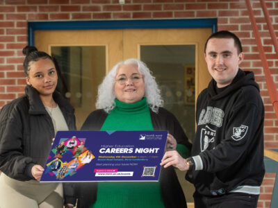 2 students and a lecturer hold up a sign promoting the Higher Education evening at NWRC
