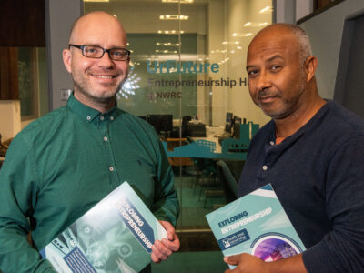 Two men standing outside an office holding an entrepreneurship book