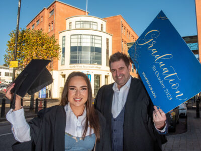 A man and woman wearing graduation gowns and mortar boards outside NWRC's Strand Road campus.