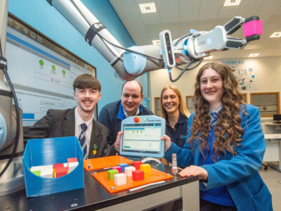 Two school pupils with a man and woman in a robotics room with equipment around them.