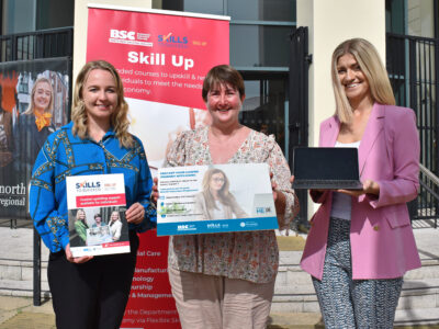 Three women pictured outside a college in the sunshine with a board advertising the women returners programme