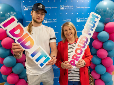 Mum and son stand in front of NWRC branding with a sign that says proud mum.